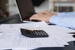 Calculator and paper bills on work table of business person using computer. Hands of professional typing on laptop, doing financial paperwork, making payments online. Close up of objects