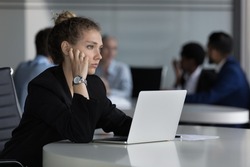 Young thoughtful woman sit at desk with laptop looks into distance feels unmotivated or unsure working on on-line task, experiences problem with solution. Challenge, corporate office workflow concept