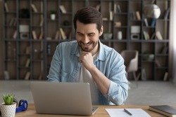 When job is pleasure. Happy millennial businessman sit at home office desk corresponding with customer using mail client on pc reading good news online. Smiling young casual guy work on laptop at web