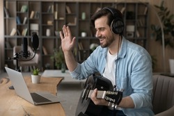 Smiling man musician vlogger influencer wave hand to laptop webcam greet channel audience before present new song with guitar. Young guy music teacher make video call to student ready to start class