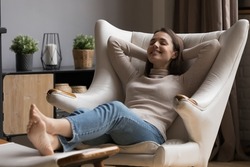 Cheerful relaxed beautiful 20s girl resting in comfortable armchair with closed eyes, peaceful smile, comfort, breathing fresh air. Smiling at good thoughts, laughing. Cozy home, relaxation concept