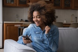 Excited cheerful gen Z African teenager girl using mobile phone, getting surprising good news, looking at screen, laughing, celebrating win, success, luck, achieve, good result