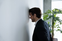 Upset businessman banging his head against wall in despair looks stressed having problems at work, bankruptcy, business failure unsuccessful negotiations, project loss, failed job interview concept