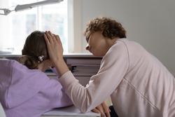 Rear view caring mother comforting upset depressed teenage daughter, touching head, expressing empathy and love, young mum supporting tired sad teen schoolgirl sitting at desk at home