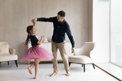 Happy daddy teaching lovely daughter in ballet skirt to dance. Pretty girl wearing princess dress training choreography skills with dads help and support. Fatherhood, family home activity concept