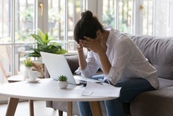 Stressed desperate broke business woman, homeowner getting frustrated at laptop at home, touching head, suffering from headache due to bad news. Financial problems, bankruptcy concept