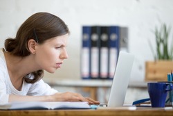 Young stressed businesswoman sitting with laptop and looking at screen with concerned facial expression. Surprised and focused business person staring at laptop computer screen worried and interested