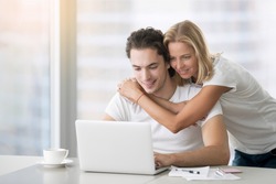 Young happy people looking at laptop, building family financial plan, meal planning for healthy style, wedding ideas, ordering gifts, free online courses to get diploma. Man working in home office
