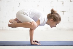 Side view of Girl child practicing yoga, standing in Crane exercise, Bakasana pose, working out wearing sportswear, t-shirt, pants, indoor full length, white loft studio background 