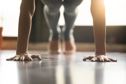Young woman practicing yoga, doing Push ups or press ups exercise, phalankasana Plank pose, working out, wearing sportswear, grey pants, indoor, home interior, living room floor. Close-up of hands 
