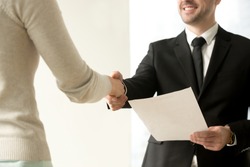 Employment handshake, smiling friendly employer shaking new hire hand, happy businessman holding document, giving official paper to businesswoman, offering job contract, focus on hands, close up view