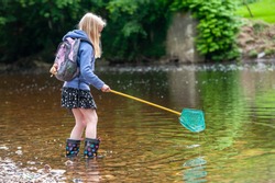 Young blonde girl wish fishing net wading into river