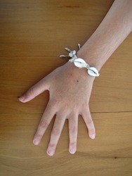 Hand of a 8-year-old girl wearing a bracelet made with conch shell and straw on a wood surface