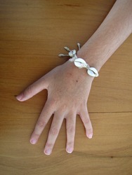 Hand of a 8-year-old girl with a bracelet made with conch shell and straw on a wood surface