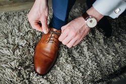 Brown leather shoe lacing. Businessman in white shirt and suit trousers. Groom getting ready for the wedding. Wearing clothes background. Dressing up male fashion.
