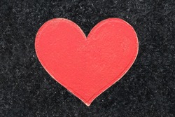 Red heart shape in stone. Black granite texture. Symbol of love graved and painted. Dark marble decorative. Valentine background. Empty copy space mineral.