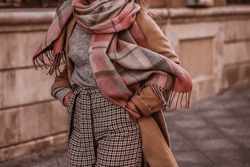 Woman in autumn stylish fashion brown long coat, scarf and plaid pants walking in the city. Female casual street style outfit. Film grain effect