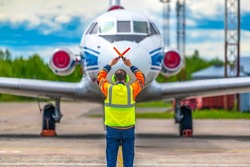 A ground crew technician in a signal vest gives a stop signal to an aircraft taxiing into the parking lot after landing for refueling, maintenance and boarding of passengers.