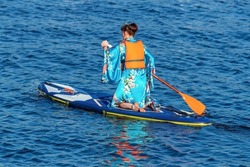 A young Asian woman in a traditional geisha costume in a boat - SUP board floats on the river with an oar in her hands.