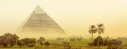 Great pyramid of Khafre in Egypt. Fantasy of egyptian landscape with ancient pyramid of Chephren in morning haze. Wide panorama in green oasis with fields and palm trees for your banner or header.