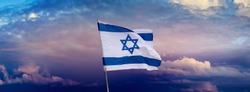 Israeli flag with a star of David over Jerusalem at cloudy sky background on sunset, panoramic view. Patriotic concept about Israel with national state symbols and copy space for wide banner.