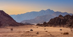 Buggy trip in a stone desert at sunset. Mountain landscape with off-road vehicles driving on a dust dirt road. Active leisure for tourists in Sharm el-Sheikh resorts, Egypt.