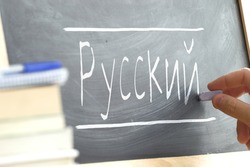 Hand writing on a blackboard in a Russian class. Some books and school materials.