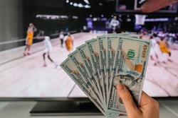 The winner at basketball betting holds a dollar money prize in hand near the TV
