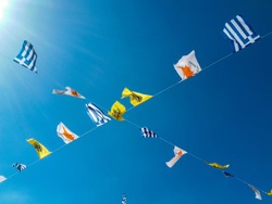 Different national flags hung on wire on a blue sky background .