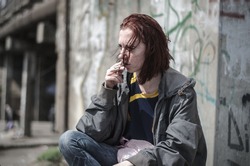 Portrait of a young girl in an old dirty, ragged clothes with dirty hair, smoking a cigarette. Disadvantaged teenager. Homeless girl.
