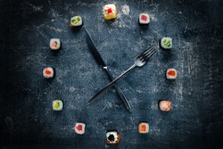 Sushi time in the form of a wall clock on a concrete background, sushi clock with fork and knife, concept of time to eat