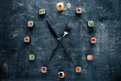 Sushi time in the form of a wall clock on a concrete background, sushi clock with fork and knife, concept of time to eat