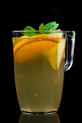 hot autumn drink with orange, apple and mint. Apple orange tea with spices and mint in a glass with pieces orange and mint on a black background