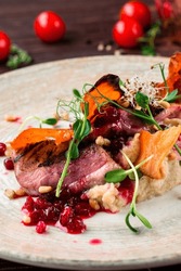 Duck breast fillets steak with parsnip and pine nuts. Fried duck fillet with parsnip puree, lingonberry sauce, sweet potato chips, herbs and pine nuts, closeup. Vertical orientation.