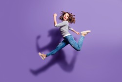 Portrait of sportive active girl in motion jumping over in the air isolated on violet background having perfect stretching looking at camera