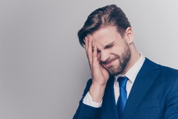 Portrait of disappointed, upset man with stubble in blue suit, cover half face with palm, isolated on grey background, forget something important to do, emotion after divorce, failure