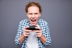 Portrait of stylish trendy attractive handsome crazy worried funny young man with wavy hair in casual checkered shirt, game addict playing video game in play-station. Isolated over grey background
