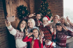 Cheerful full family showing two finger festure v-sign. Noel gathering. Cheerful grandparents grandchildren sister brother, son daughter taking self photo, photographing on mobile cell cellphone phone