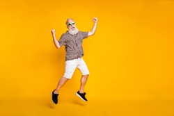 Full length photo of funny funky lucky old bearded man in green eyewear eyeglasses raise fists scream yeah celebrate victory jump wearing leopard shirt shorts isolated over yellow background