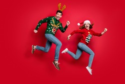 Full length photo of crazy jumping couple excited by x-mas discounts prices wear ugly ornament jumpers isolated red color background