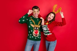 Portrait of funky crazy two people  wife husband in brown antlers costume lean shoulder wear denim seasonal clothes christmas tree design pullover jumper spectacles isolated over red color background