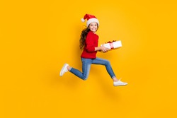 Full size profile photo of crazy little lady jumping high taking giftbox from santa in x-mas midnight wear red knitted pullover and jeans isolated yellow background