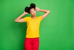 Photo of amazing dark skin lady holding arms on modern youth hairdo sending air kisses shy looking empty space wear casual yellow t-shirt and red pants isolated green background