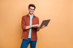 Portrait of his he nice attractive cheerful cheery successful content smart clever brunet guy agent broker holding in hands laptop working isolated over beige color pastel background
