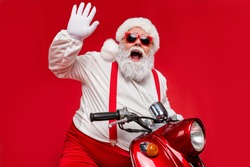 Portrait of his he nice bearded cheerful cheery funky Santa hipster riding motor bike spending December vacation congratulating you isolated on bright vivid shine vibrant red color background