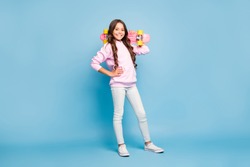 Turned full length body size photo of cheerful pink positive girl holding skate board on her shoulder wearing footwear isolated pastel blue color background