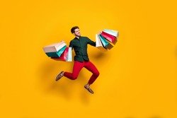 Full length body size photo of cheerful positive handsome jumping man holding numerous packages returning from shopping mall isolated vivid color background