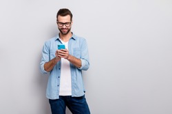 Photo of attractive macho guy perfect appearance neat hairstyle easy-going person holding browsing telephone wear specs casual denim outfit isolated grey color background