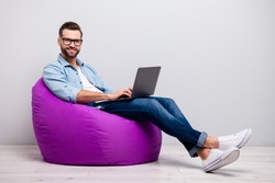 Full body profile photo of funny guy holding notebook browsing chatting colleagues sitting comfy soft armchair wear specs casual denim outfit isolated grey color background