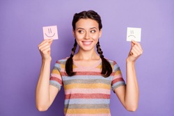 Photo of funny lady holding paper emoticons good and bad mood picking positive emotions wear casual striped t-shirt isolated pastel purple color background